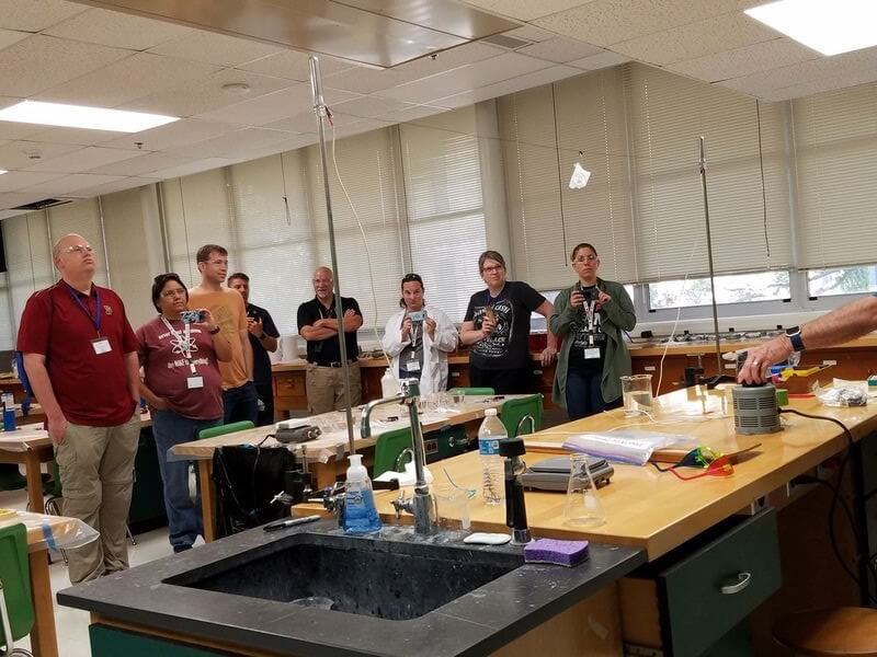 A group of ASM teachers watches an experiment involving paper on a wire