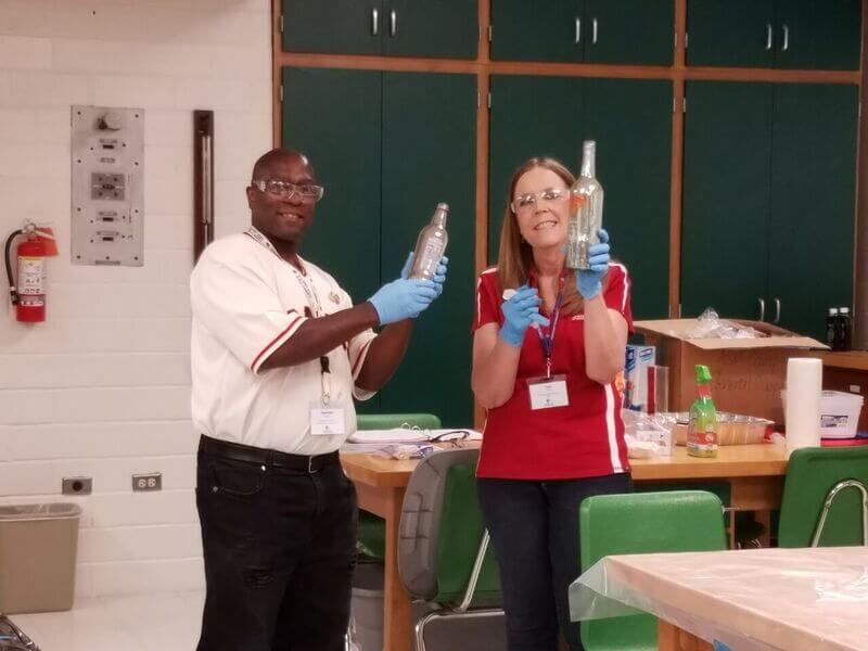 Two ASM teachers hold up bottles while conducting an experiment at summer camp