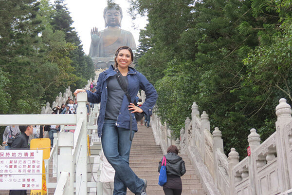 A female student stands at the bottom of a staircase leading to a giant Buddha statue