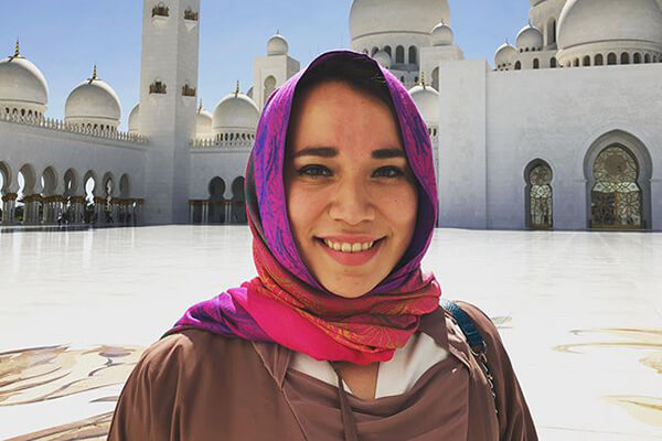 A female student studying in Dubai smiles in front of Middle Eastern buildings