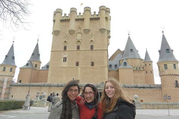Three students stand in front of a castle in Alcala, Spain