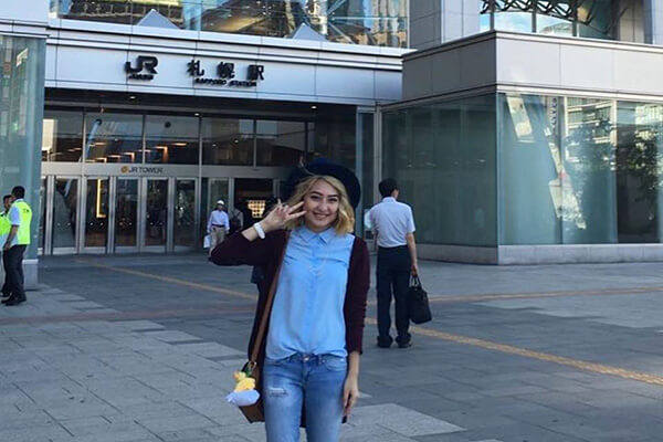 Female student smiles in front of a building with a Japanese logo
