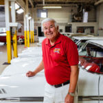 Car collector stands in front of his cars in his garage.
